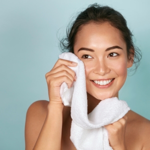 Washing face. Closeup of woman cleaning skin with towel portrait. Beautiful asian girl model wiping facial skin with soft facial towel, removing makeup. High quality studio shot